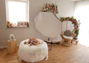 Heller Studioraum mit Softbox, gepolstertem Fotoplatz, Blumen und einem Korbstuhl