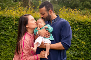 Ein Paar hält sein Baby im Garten im Arm und küsst es liebevoll auf den Kopf und die Wange
