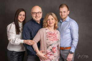 Vier Erwachsene stehen eng beieinander und lächeln vor einem dunklen Studiohintergrund