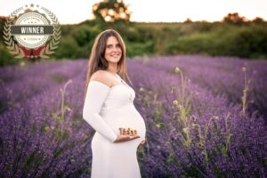 Schwangere Frau im weißen Kleid im Lavendelfeld mit Schriftzug Liebe und AFNS-Award-Winner-Siegel Juli 2024