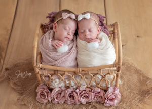 Zwei schlafende Babys mit Schleifen im Haar in einem kleinen Korbbett mit Rosen