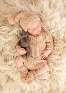 Schlafendes Baby mit beiger Zipfelmütze und Strickanzug auf einer flauschigen Decke