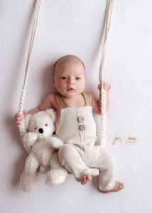 Waches Baby mit weißem Teddybären auf einer gepolsterten Seilschaukel
