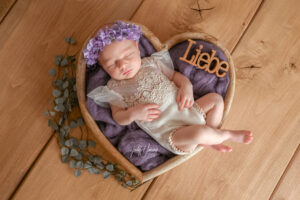 Schlafendes Baby mit violettem Blumenkranz in einer herzförmigen Schale mit dem Schriftzug Liebe