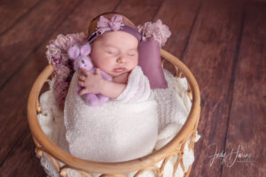 In ein weißes Tuch gewickeltes Baby mit violettem Blumenkranz in einem Korb