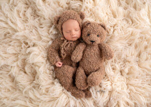 Schlafendes Baby in braunem Strickanzug mit einem Teddybären auf einer weichen Decke